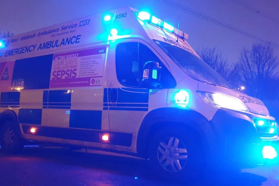 Full view from font side of an ambulance with blue lights on at night time.