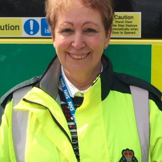 a photo of a lady with short hair, a fluorescent jacket stood in front of an ambulance vehicle