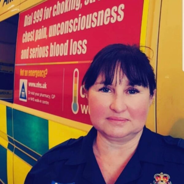 a dark haired lady in ambulance uniform stood at the side of an ambulance