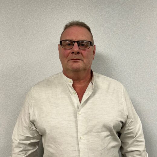 a man in a white shirt in front of a plain wall wearing glasses