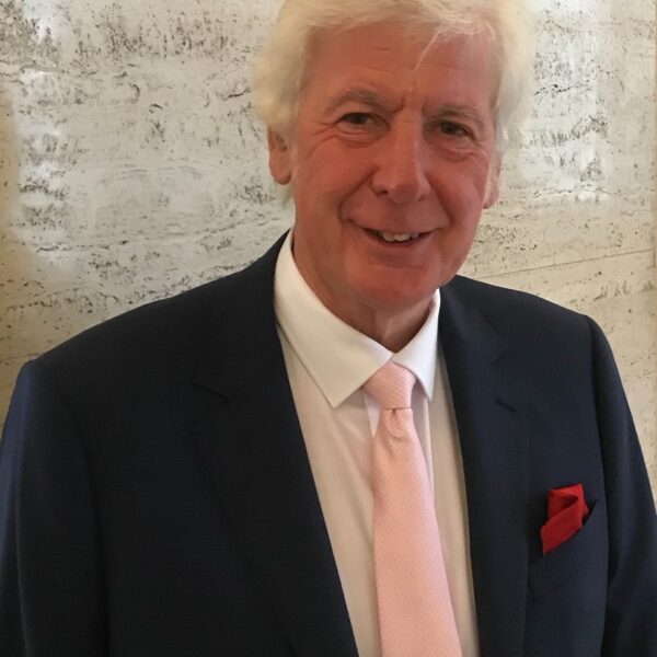 a man stood in front of a textured wall, wearing a suit with a pink tie