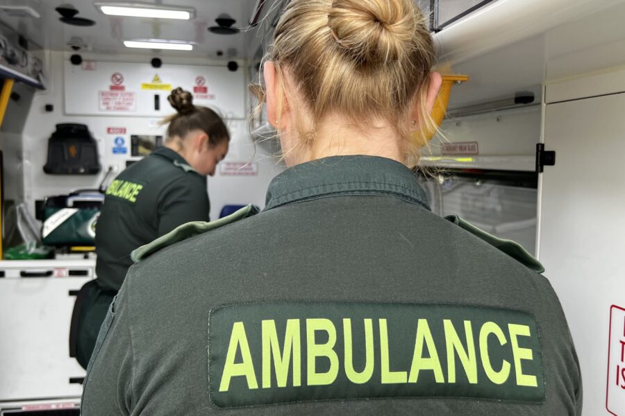 Over the shoulder photo of female ambulance crew in back of ambulance treating patient on stretcher